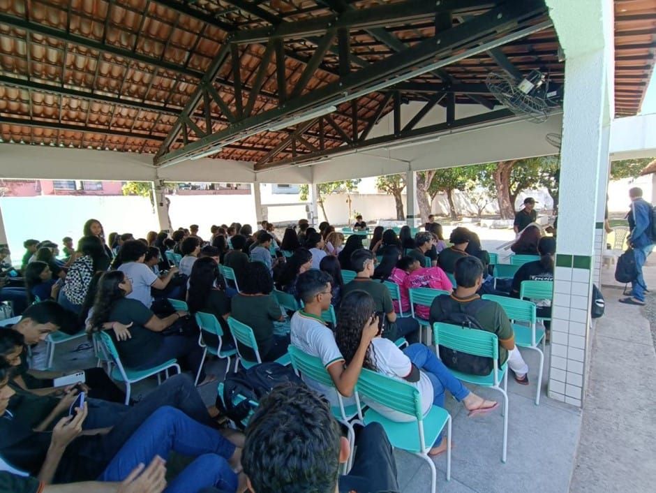 Alunos na Assembleia estudantil sentados em cadeiras em uma quadra.