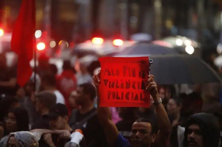 Homem segura cartaz dizendo "Pelo fim da violência policial" em protesto